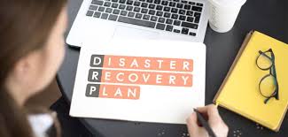 A person reviewing a document labeled 'Disaster Recovery Plan' next to a laptop and notebook, symbolizing tips for financially managing a business post-disaster.